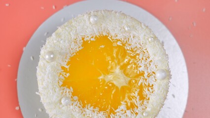 Cake with orange and coconut shavings spun on a pink background.