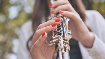 A girl plays the clarinet in the summer in the park. Close-up of her hands.