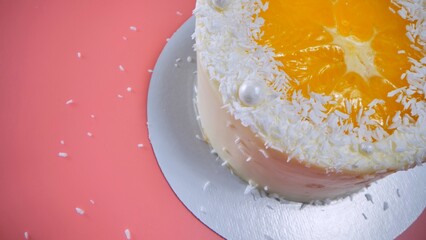 Cake with orange and coconut shavings spun on a pink background.
