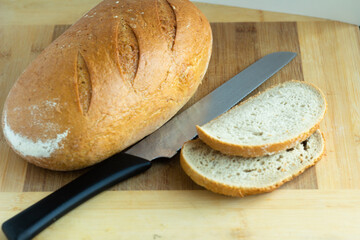 white wheat bread with slanting cuts with cut pieces and a knife on a wooden background
