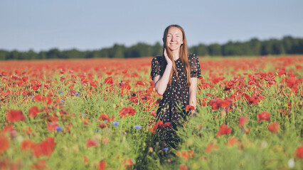 A young girl walks through a red poppy field.