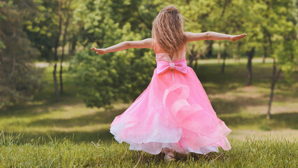 A girl in a pink princess dress is spinning in the park.