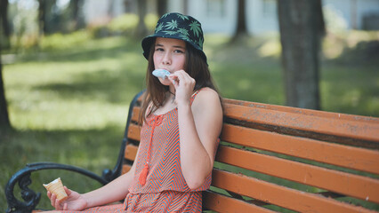 Teenage girl eating ice cream in the park on the bench.