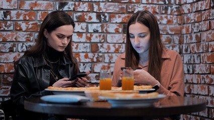 Two beautiful girls are sitting in a cafe and talking with phones.