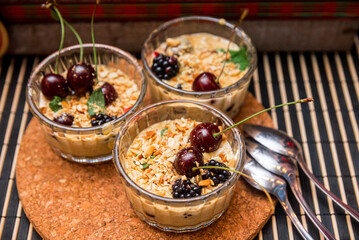 Three servings of vanilla cream dessert with crushed peanuts and fresh blackberries and cherries