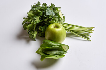 some green vegetables on a white surface, including an apple and ceince leaves with parise in the background