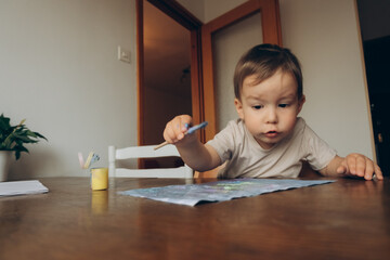 the child draws with a brush and multicolored gouache sitting at the table drawing to his mother
