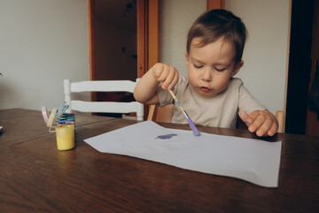 the child draws with a brush and multicolored gouache sitting at the table drawing to his mother