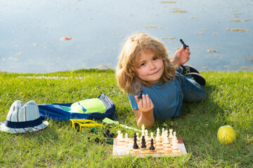 Kid shows chess pieces on a chessboard. Early development. Boy thinking about chess in summer park....