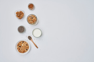 some food that is on a white surface with spoons and bowls filled with different types of cereal, nuts, milk, and other ingredients