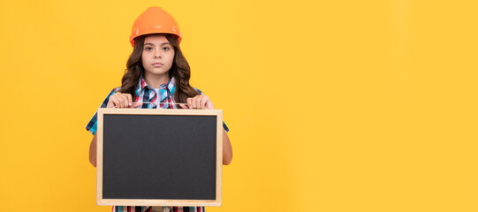 Builder teenager girl in helmet. serious child in helmet presenting school blackboard with...