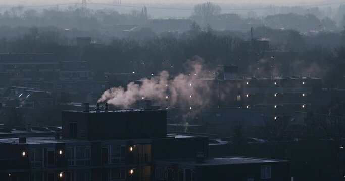 Densely built urban scenery with smoking chimneys on an early winter morning. Extremely long shot, warm air distortion visible above the buildings.