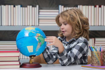 School kid pupil looking at globe in library at the elementary school. World globe. School child 7-8 years old with book go back to school. Little student.