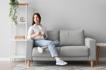 Young woman with cup of hot beverage sitting on sofa at home