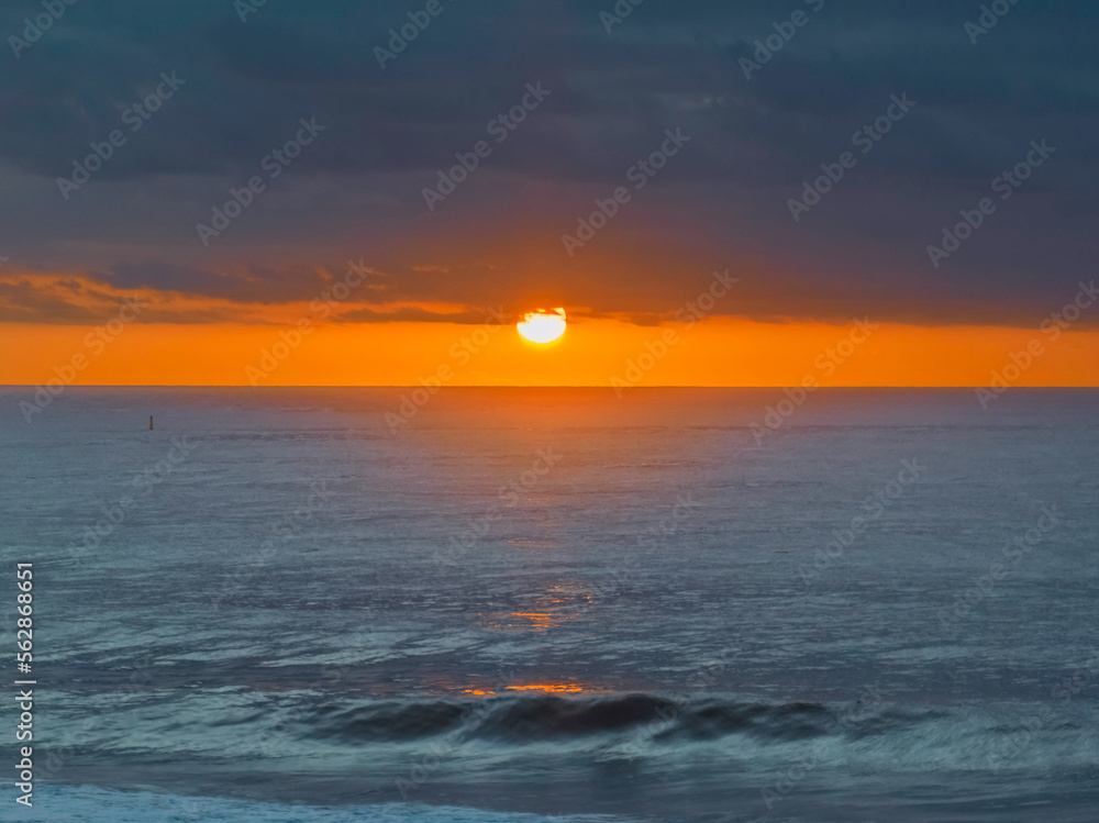 Wall mural sunrise over the blue sea with big bold sun under the clouds