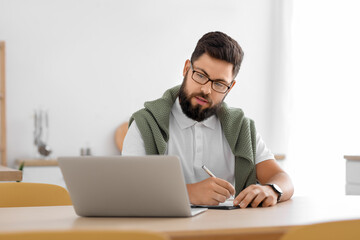 Male psychologist with laptop video chatting at table in kitchen