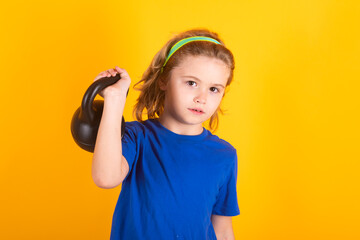 Sporty kids, studio isolated portrait on yellow background. Child boy pumping up biceps muscles with kettlebell. Fitness kids with dumbbells.