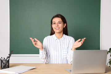Happy young teacher explaining something at table in classroom