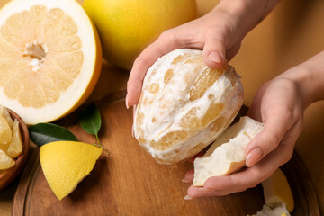 Female hands with peeled pomelo on wooden board, closeup
