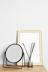 Stylish mirror, reed diffuser and picture frame on table near light wall