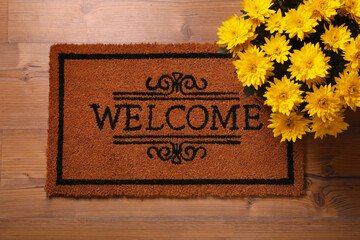 Naklejka premium Doormat with word Welcome and beautiful flowers on wooden floor, flat lay