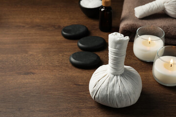 Fototapeta na wymiar Herbal massage bag, spa stones and candles on wooden table. Space for text