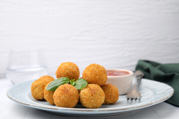 Plate of delicious fried tofu balls with basil and sauce on white tiled table