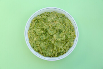 Delicious guacamole made of avocados on light green background, top view