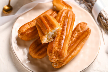 Plate of tasty eclairs on light background, closeup