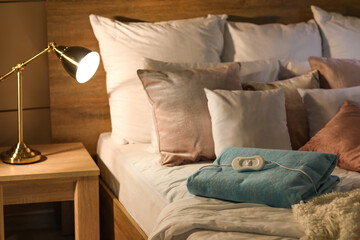 Bed with pillows and folded electric heating pad in bedroom at night © Pixel-Shot
