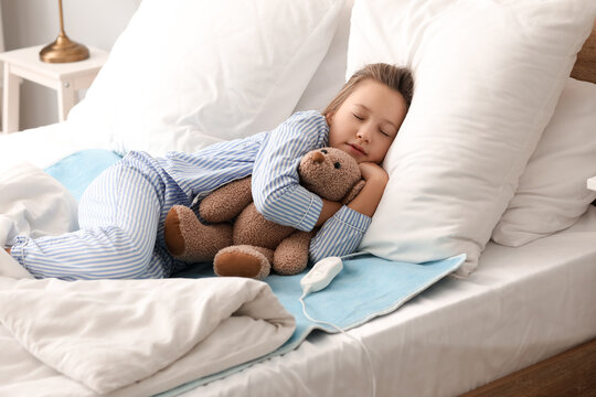 Little girl with toy sleeping on electric heating pad in bedroom
