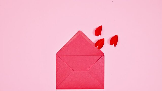 Flying hearts with wings enter in red envelope on pastel pink background. Flat lay. Stop motion