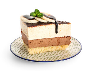 Plate with piece of birds milk cake, banana slices and chocolate topping on white background