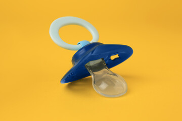 One blue baby pacifier on orange background, closeup