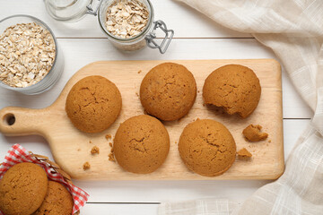 Delicious oatmeal cookies and flakes on white wooden table, flat lay