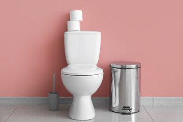 Ceramic toilet bowl, bin and paper rolls near pink wall