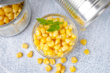 Tin cans, bowl with corn kernels and parsley leaf on grey table