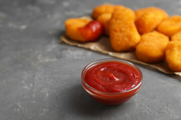 Tasty chicken nuggets with ketchup on grey table, closeup. Space for text