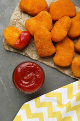 Tasty chicken nuggets with ketchup on grey table, top view