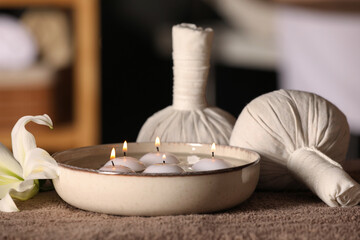 Fototapeta na wymiar Spa composition with burning candles, lily flower and herbal bags on massage table in wellness center, closeup