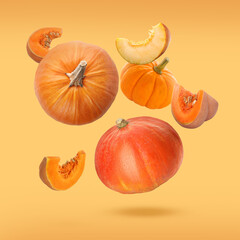 Whole and cut pumpkins falling on orange background