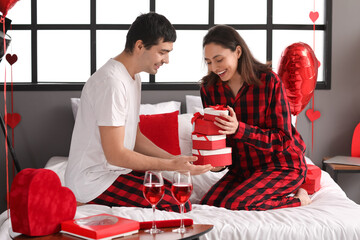 Young couple with gifts in bedroom on Valentine's Day