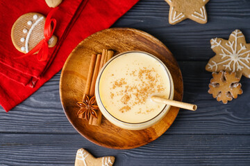 Glass of tasty eggnog cocktail, spices and Christmas cookies on dark wooden background