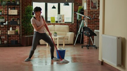 Happy funny person mopping floors with all purpose cleaner and dancing, spring cleaning. Young cheerful housewife using mop to sweep dirt and clean mess, listening to music at home.