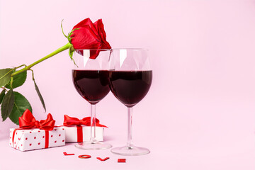 Glasses of wine, rose flower and gift boxes on pink background. Valentine's Day celebration