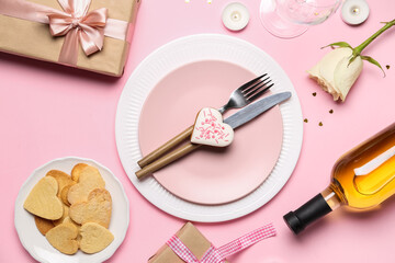 Table setting with bottle of wine, glasses, rose flower, cookies and gifts on pink background. Valentine's Day celebration