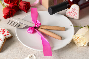 Plate and cutlery tied with pink ribbon on light table. Valentine's Day celebration