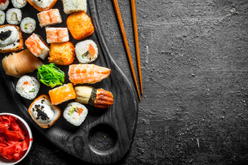 Sushi and rolls on a cutting Board with ginger and chopsticks.
