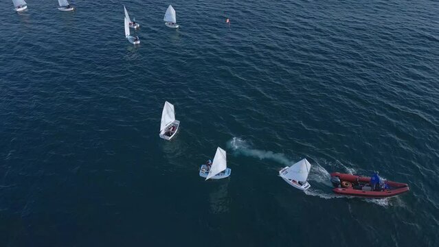 Junior sailors sport competition. Junior yacht club regatta in the open sea, teachers boat make a turn. Junior training course on sailboats. Aerial drone video slow motion footage. 