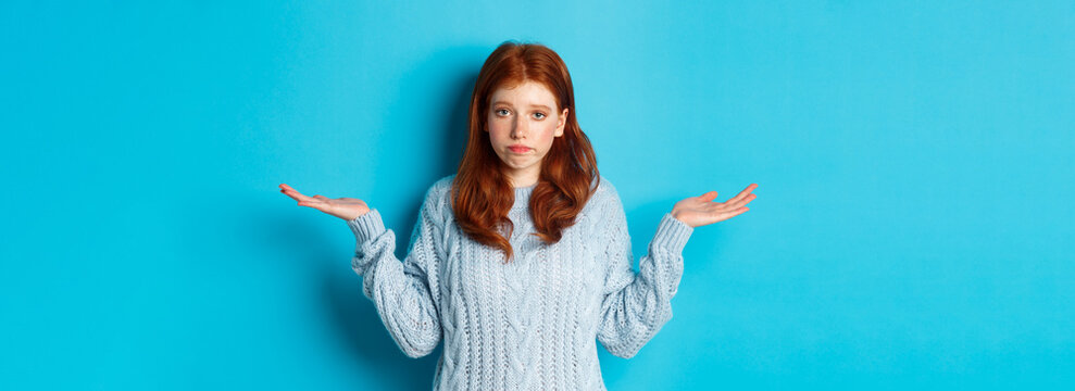 Clueless Redhead Girl Shrugging And Saying Sorry, Standing Puzzled Against Blue Background, Have No Idea